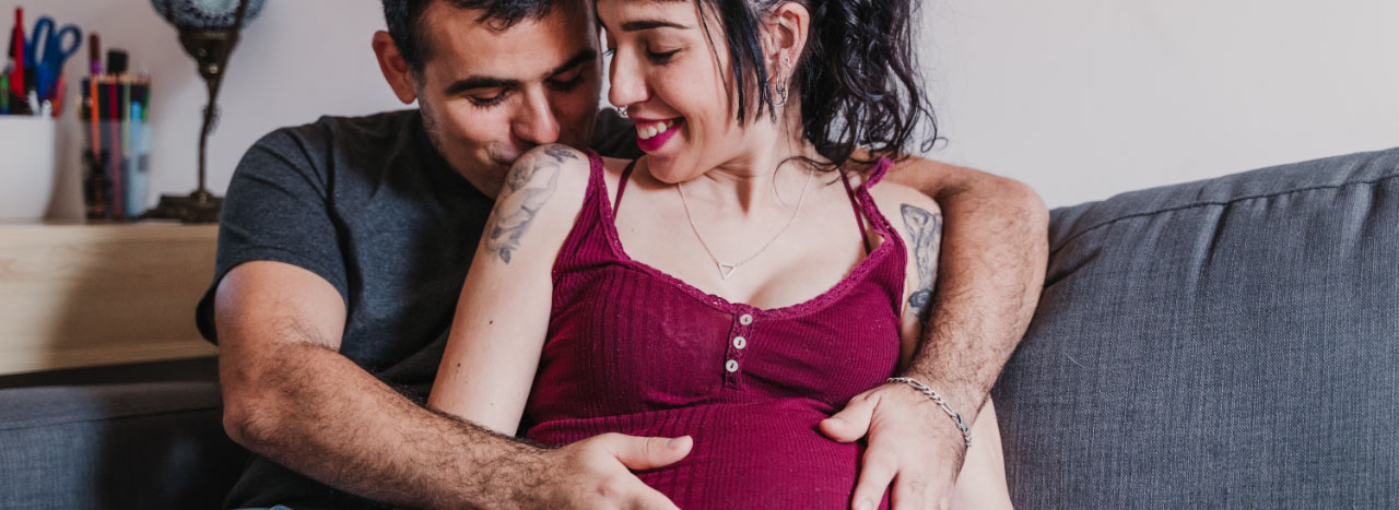 Man kisses woman's shoulder while embracing her pregnant belly